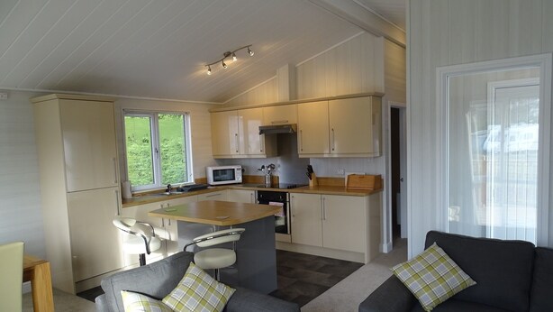 A modern kitchen with a central island, built-in appliances, and a dining area with grey sofas and plaid cushions.