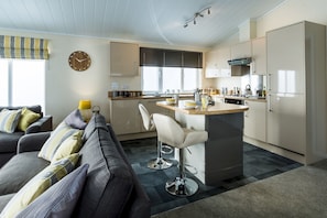 Una cocina moderna con una isla central, un área de comedor con sofá y un amplio ventanal con persianas.
