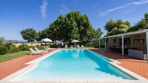 Une piscine rectangulaire à l’eau d’un bleu limpide, entourée d’une terrasse carrelée. Des chaises longues et des parasols sont disposés le long du bord de la piscine.