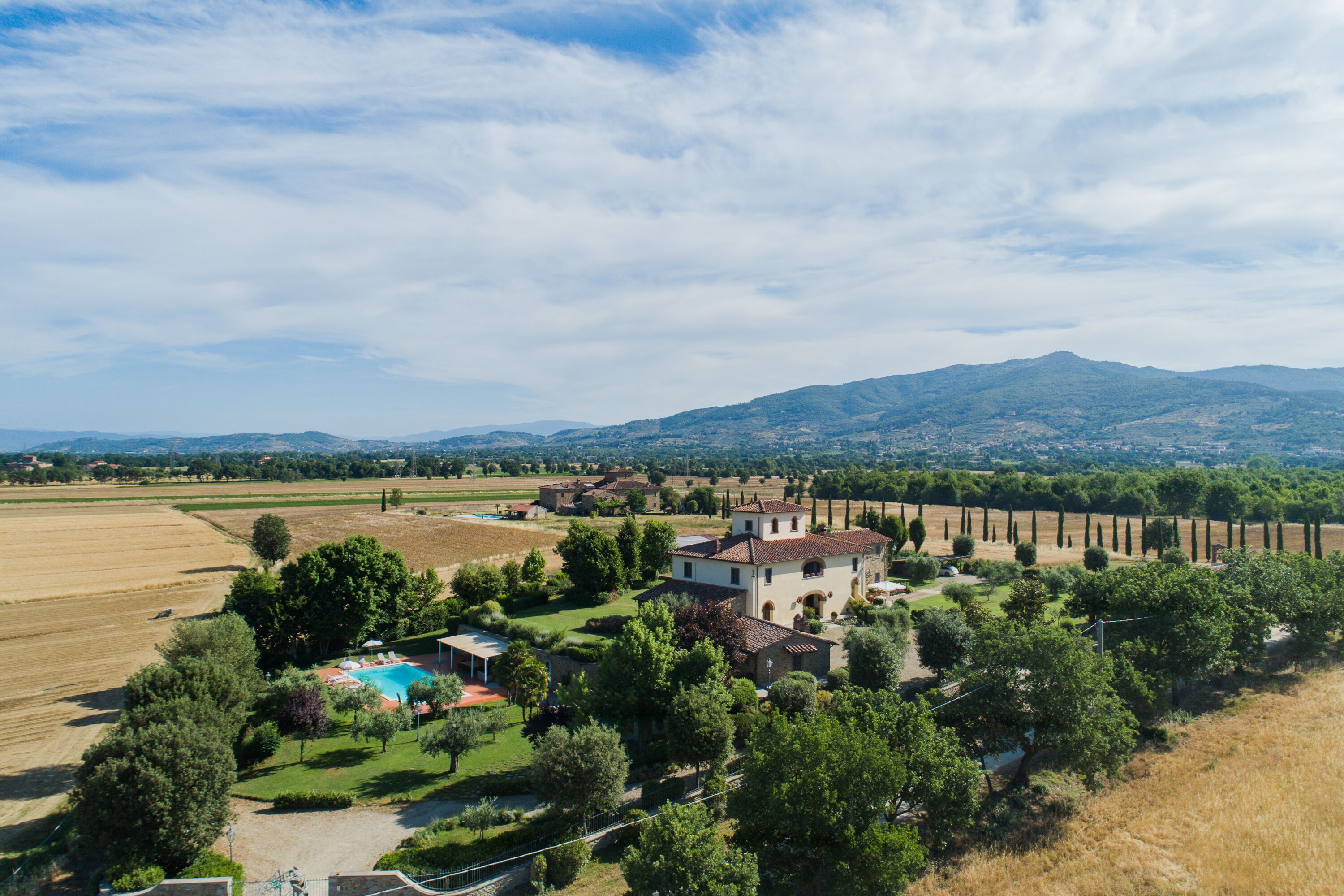 Una propiedad rural con una casa grande rodeada de campos, una piscina y una montaña al fondo.