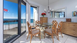 A dining area with wicker chairs and a glass table, overlooking a beach.