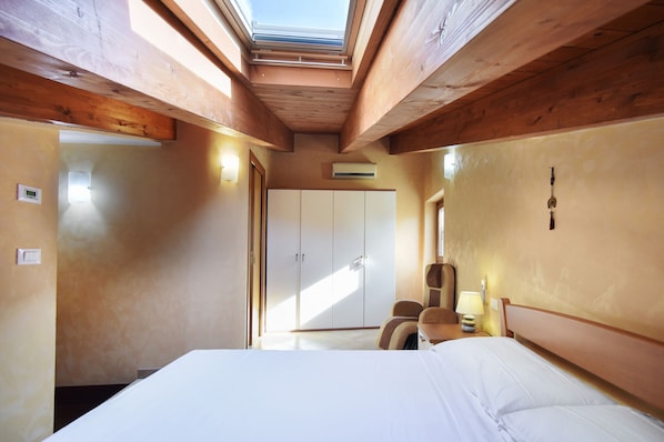 A bedroom with a skylight, a bed, a chair, and a wardrobe.