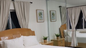 Una cama bien hecha con sábanas blancas, un cabecero de madera y una mesita de noche con una planta.