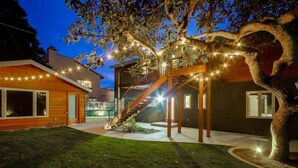 Ein modernes Haus mit Holzfassade, einer Treppe zu einer Terrasse und Lichterketten.