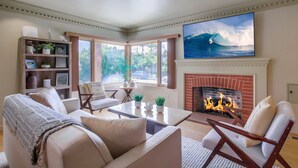 Ein Wohnzimmer mit Kamin, gemütlicher Sitzgruppe, Bücherregal und großem Fernseher, der einen Surfer zeigt.