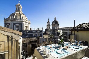 Terraço no telhado com mesa posta para café da manhã, com vista para edifícios históricos com cúpulas e torres.
