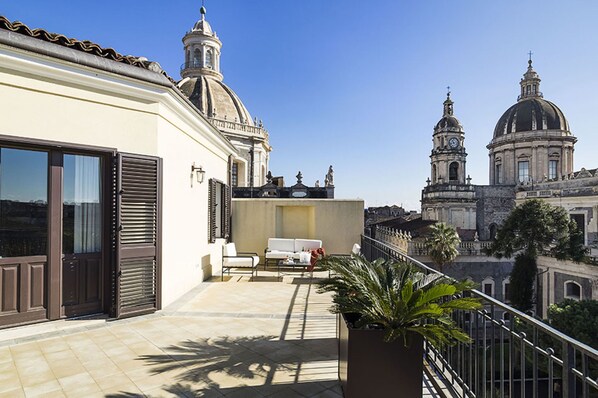 Varanda com sofá e planta em vaso, com vista para edifícios históricos com cúpulas e torres.