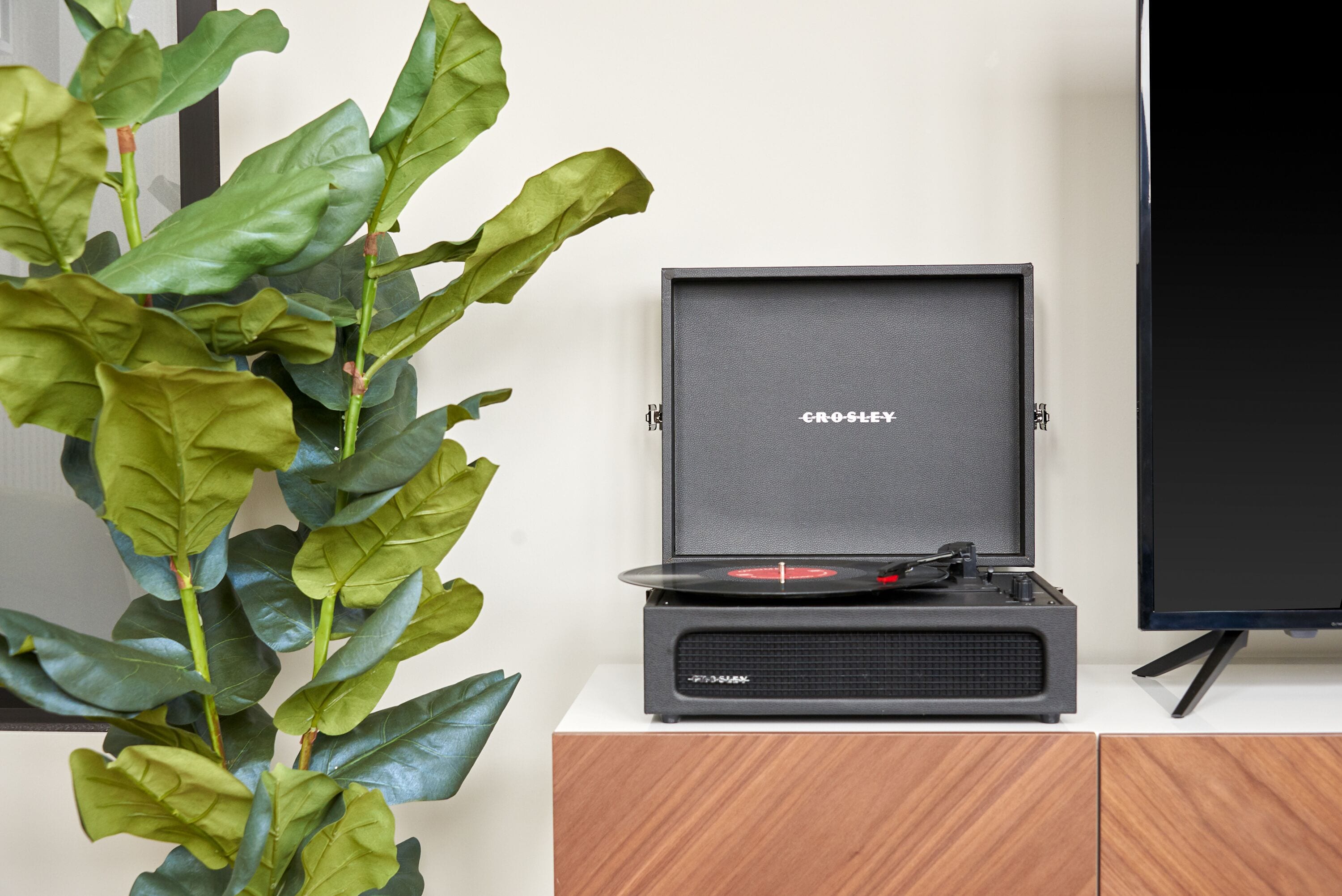 A Crosley turntable on a wooden cabinet with a plant beside it.