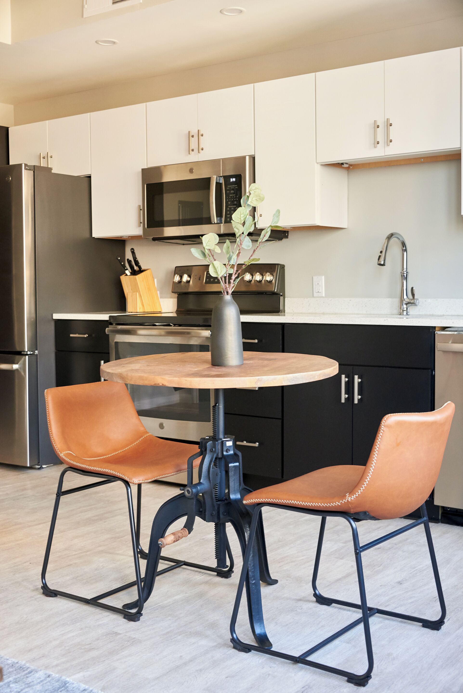 A modern kitchen with white cabinets, stainless steel appliances, a round wooden table, and two leather chairs.