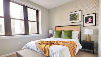 Ein Hotelzimmer mit Bett, Fenster, Nachttisch und einer Wand mit Kunstwerken.