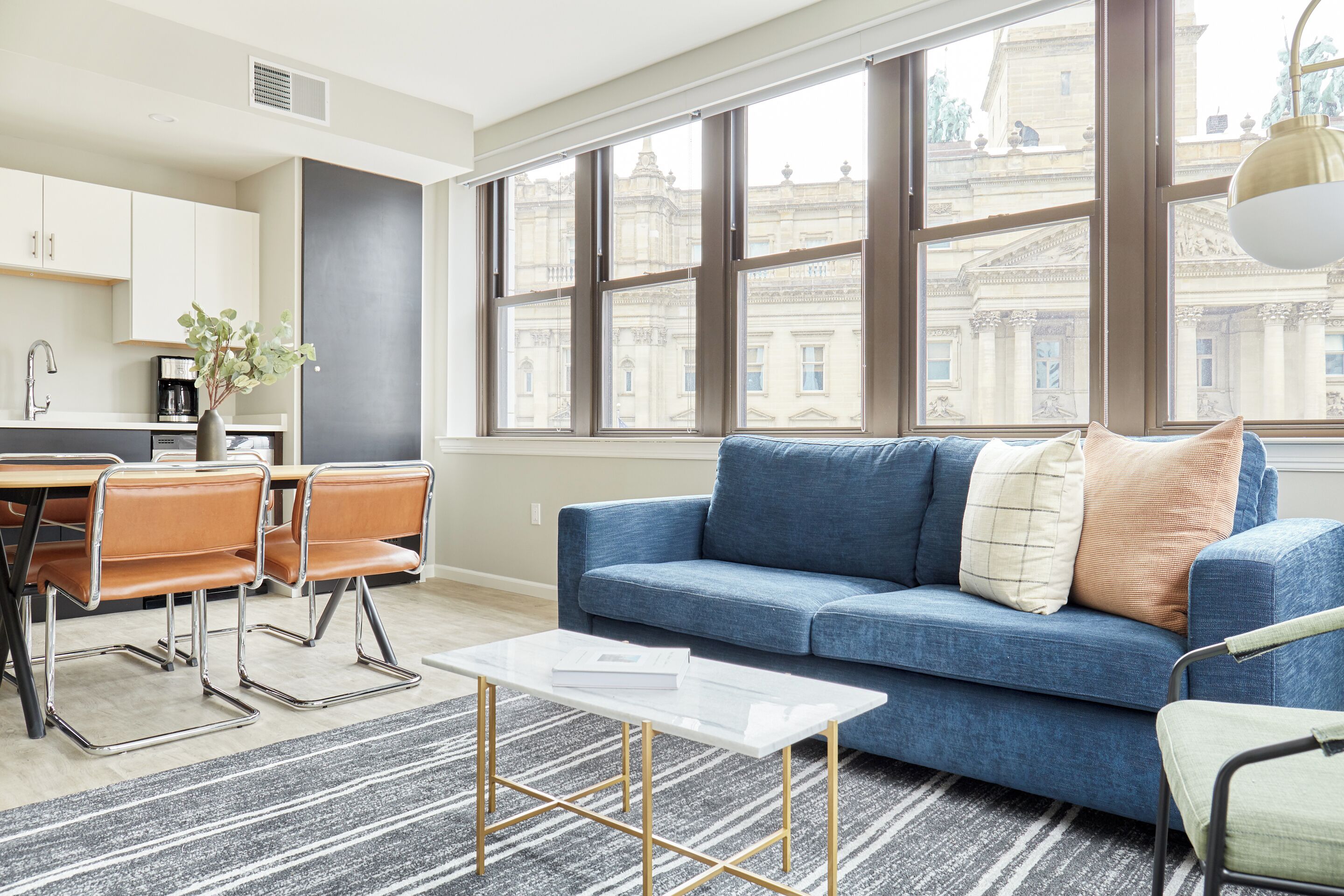 A modern living room with a blue sofa, a coffee table, and a dining area with a table and chairs.