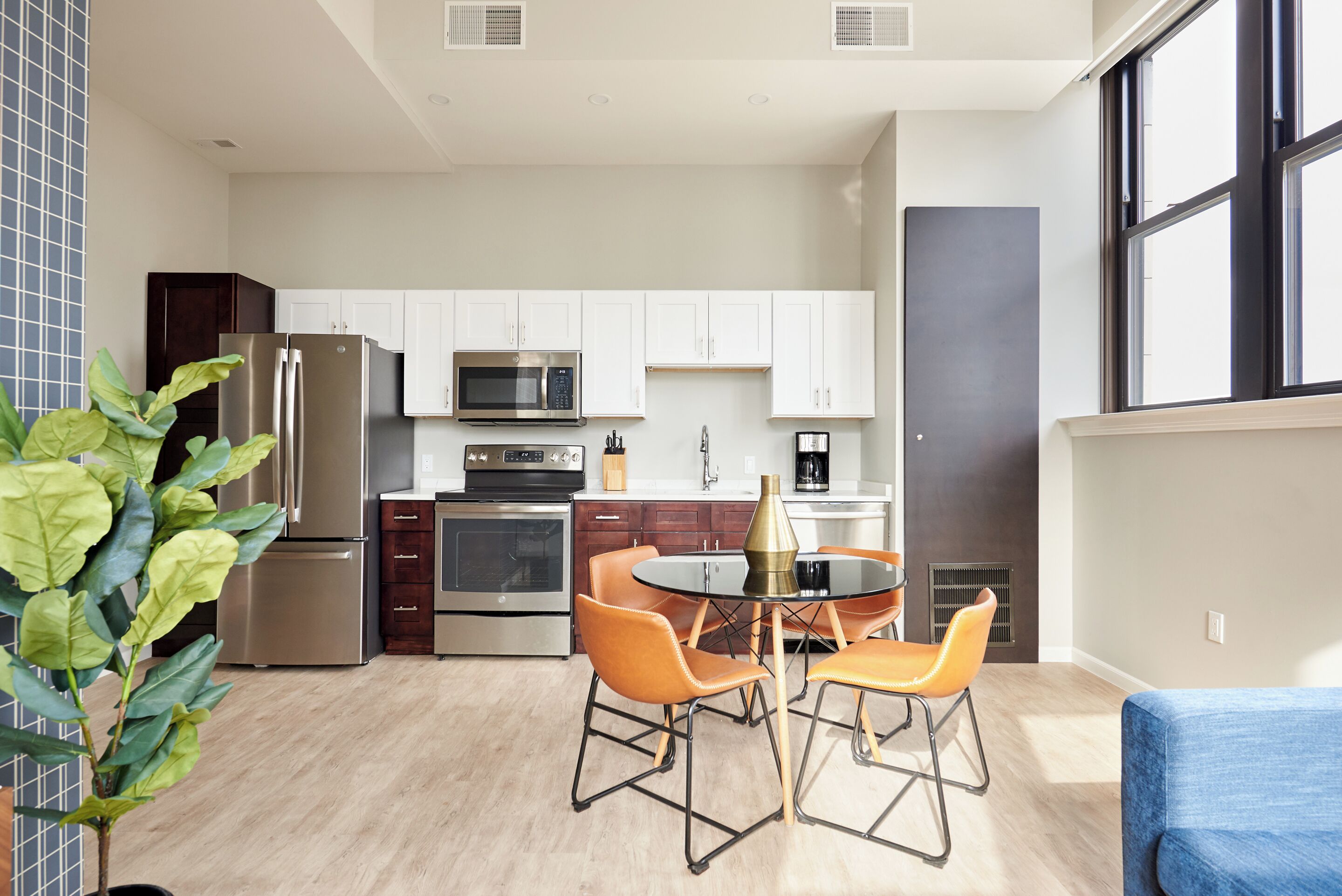 A modern kitchen with white cabinets, stainless steel appliances, and a dining area with orange chairs.