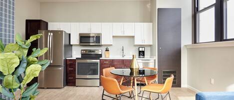 A modern kitchen with white cabinets, stainless steel appliances, and a dining area with orange chairs.