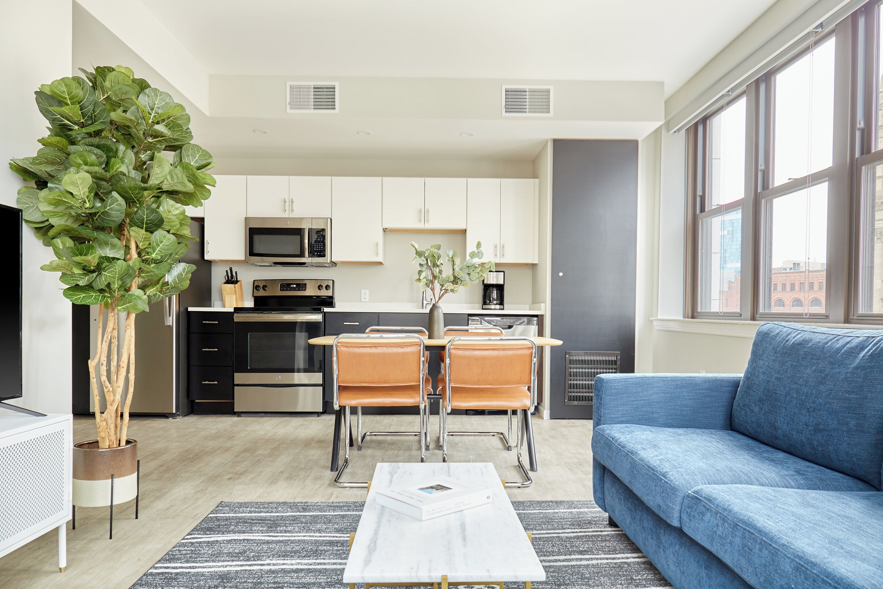 A modern living room with a blue sofa, a coffee table, and a dining area with a table and chairs.