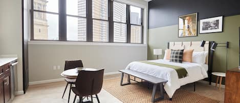 A modern bedroom with a large window, a bed, a bedside table, a chair, and a small table.