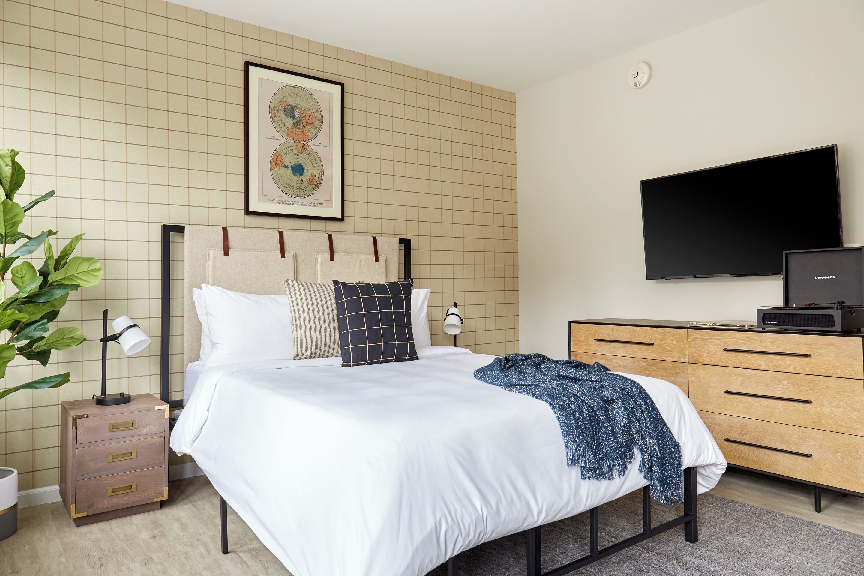 A modern bedroom with a bed, a dresser, a television, and a map on the wall.