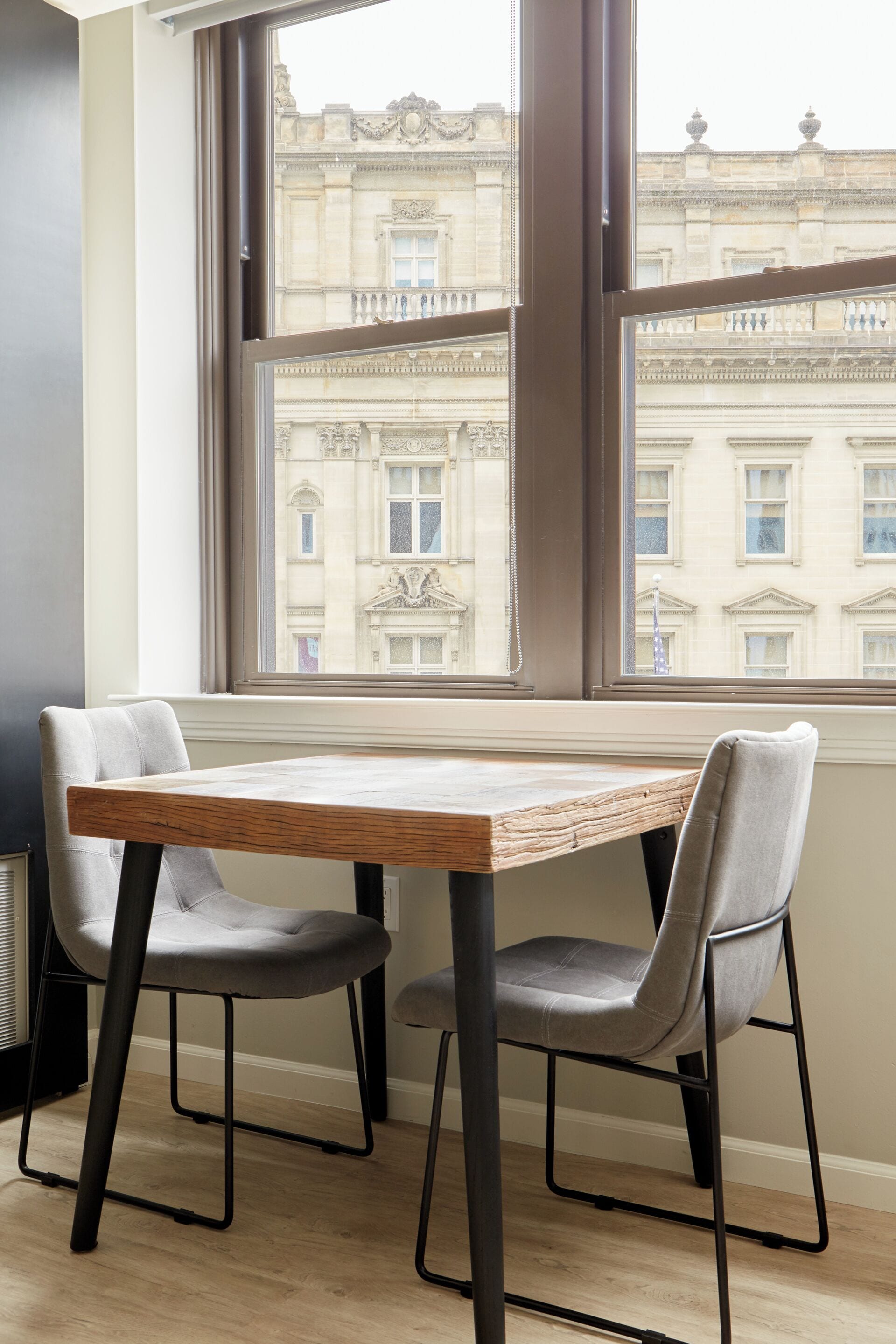 Una habitación con una mesa y dos sillas cerca de una ventana que da a un edificio.