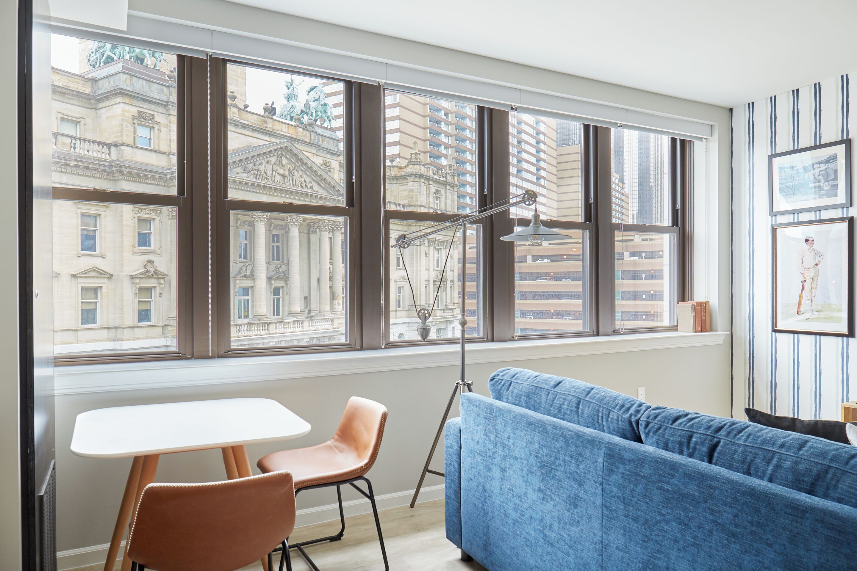 A modern living room with a large window, a blue sofa, a white table, and a floor lamp.