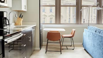A modern kitchen with a built-in oven, a dining area with a table and two chairs, and a large window with a view of buildings.