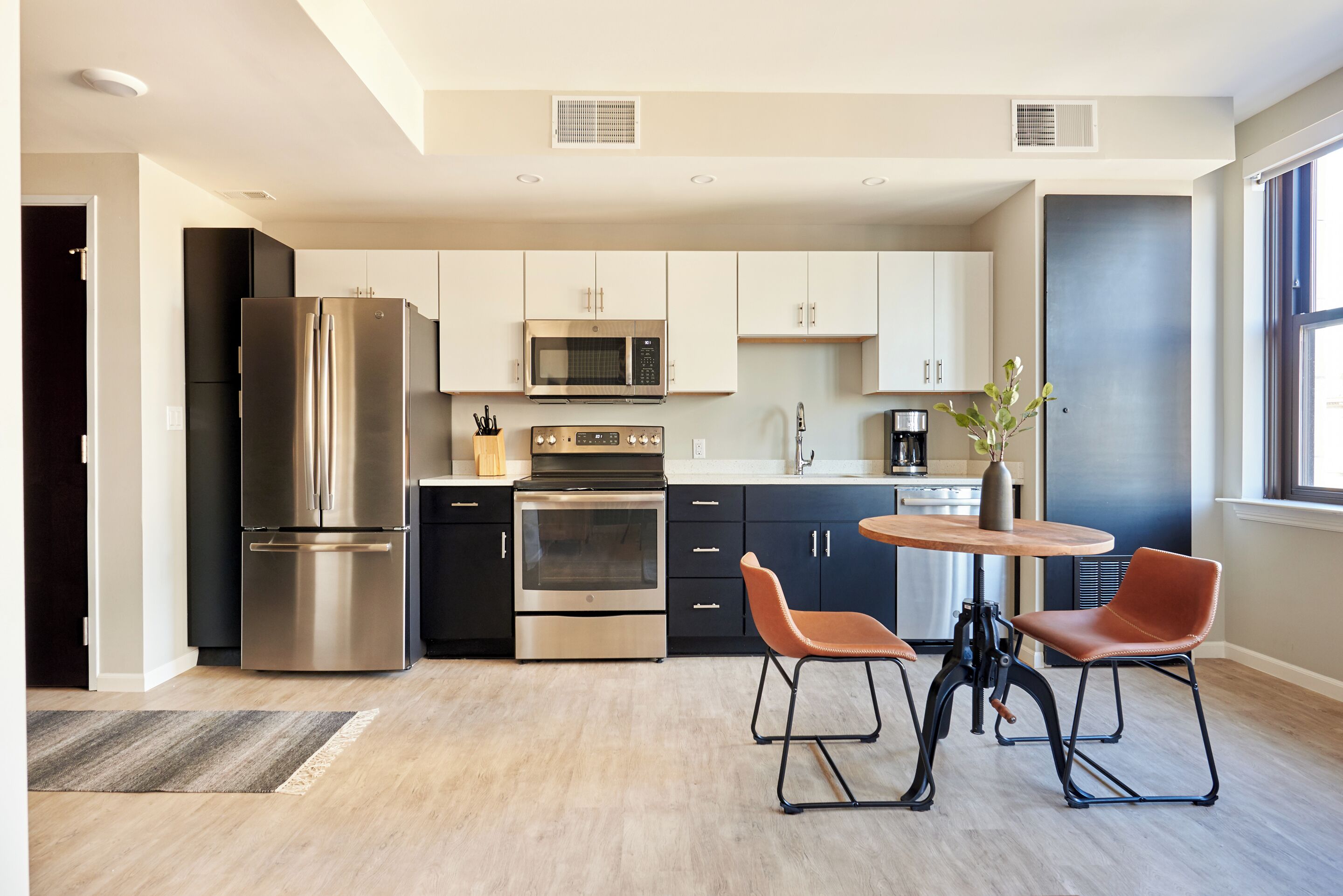 A modern kitchen with stainless steel appliances, black cabinets, and a round wooden table with two chairs.