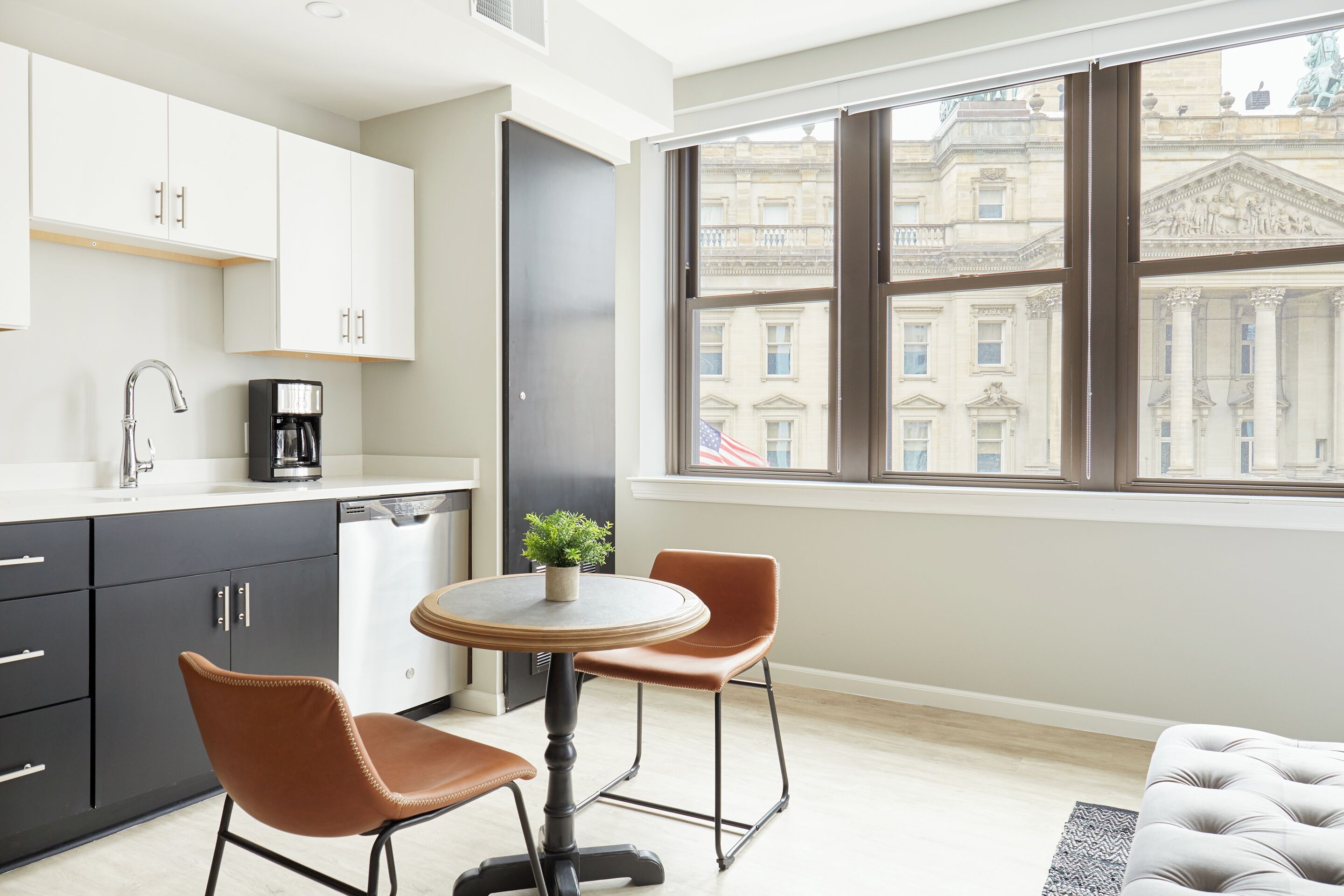 Une cuisine moderne avec un coin repas, une machine à café et une vue sur un bâtiment historique, visible à travers une grande fenêtre.