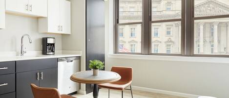 A modern kitchen with a dining area, a coffee machine, and a view of a historic building through a large window.