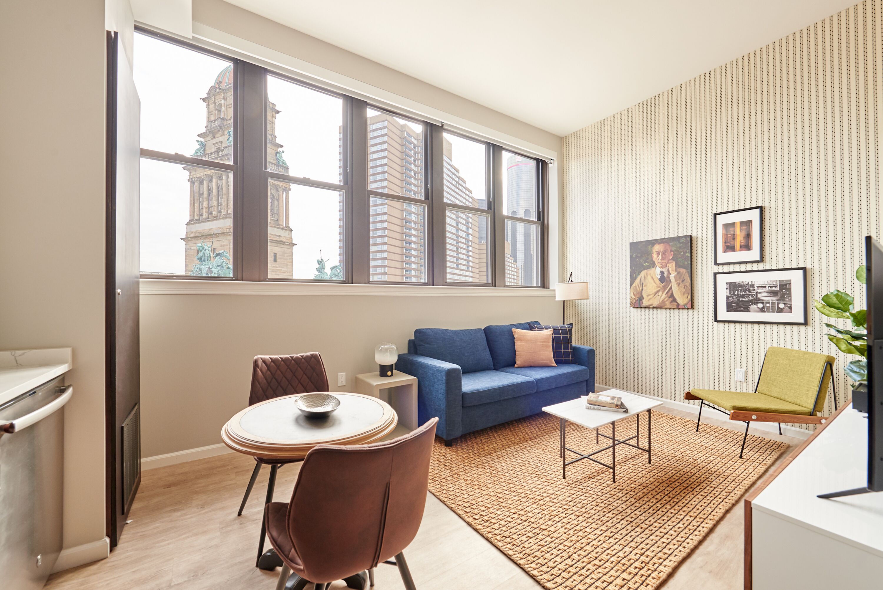 A modern living room with a large window, a blue sofa, a dining table, and a green chair.