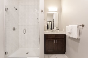A bathroom with a shower, a sink, a mirror, and a towel rack.