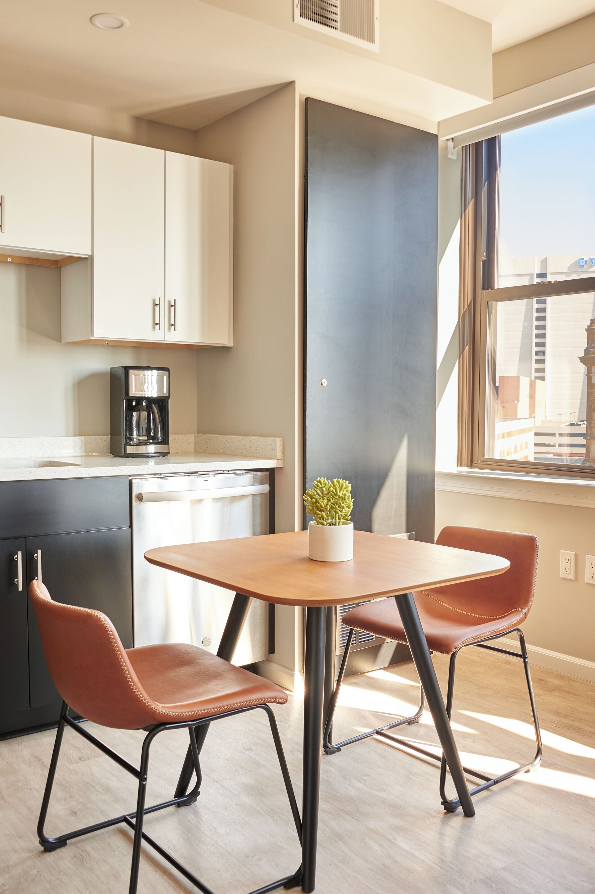 A modern kitchen with a coffee maker, a dining table with chairs, and a window with a view of buildings.