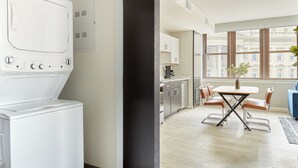 Una cuina moderna amb electrodomèstics integrats, una zona de menjador amb taula i cadires, i grans finestres que ofereixen vista a la ciutat.