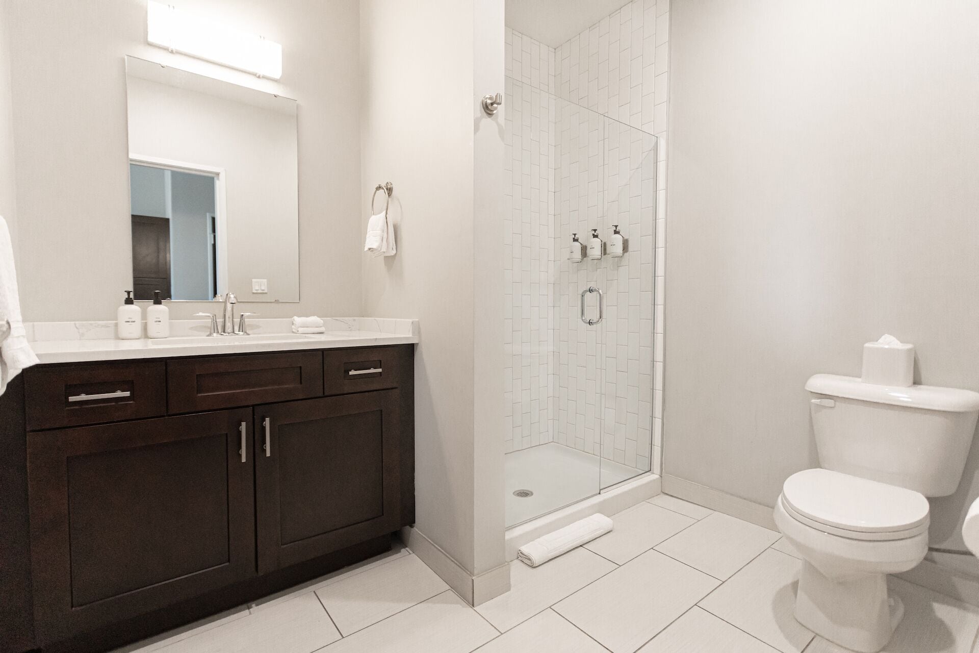 A modern bathroom with a dark wood vanity, a glass shower enclosure, and a white toilet.