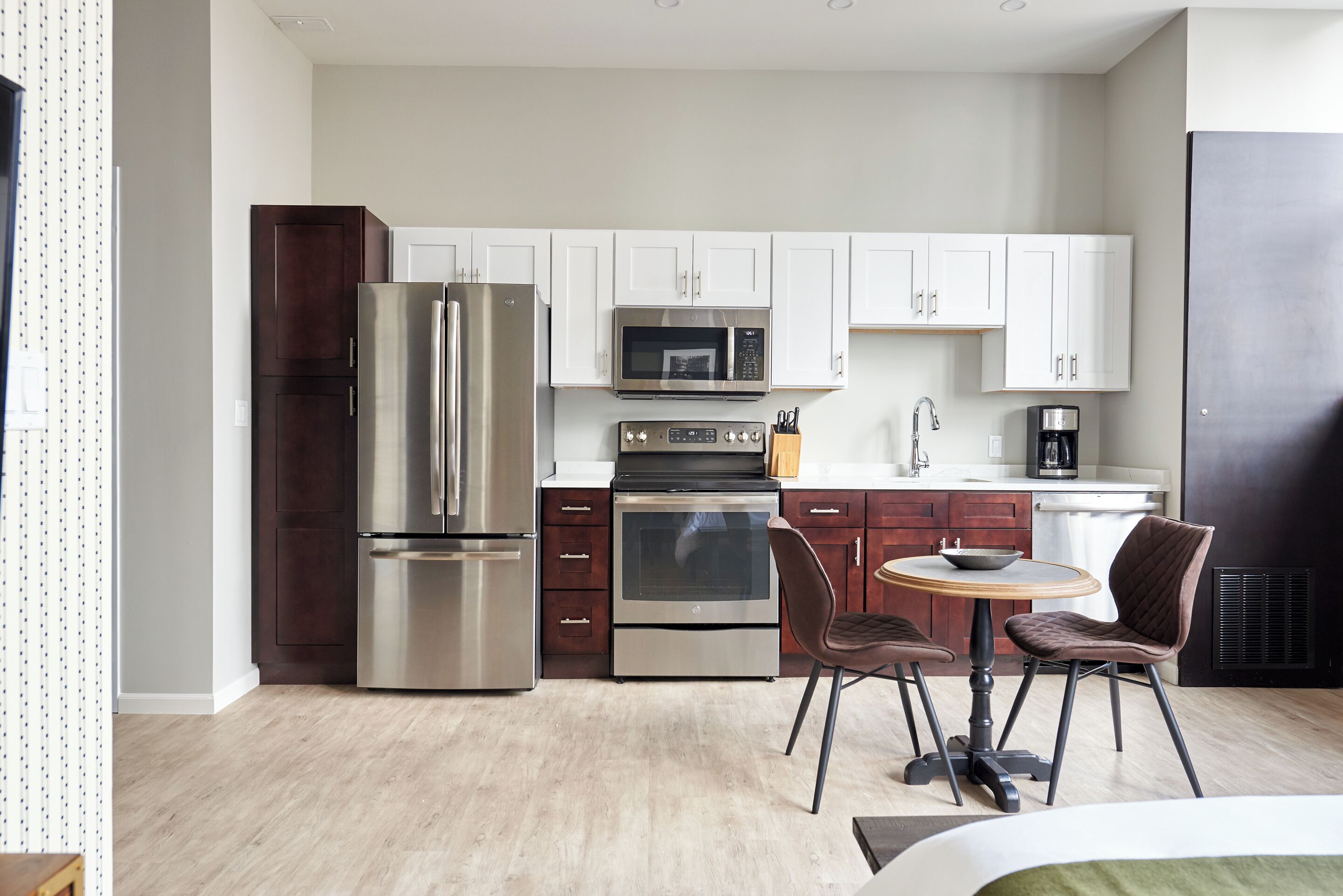 A modern kitchen with stainless steel appliances, white cabinets, and a dining area with two chairs.