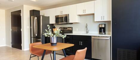 A modern kitchen with stainless steel appliances, white cabinets, and a dining area with two chairs and a table.