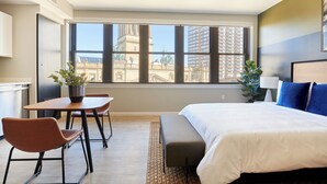 Una habitació d'hotel amb una finestra gran, un llit, un escriptori i dues cadires.