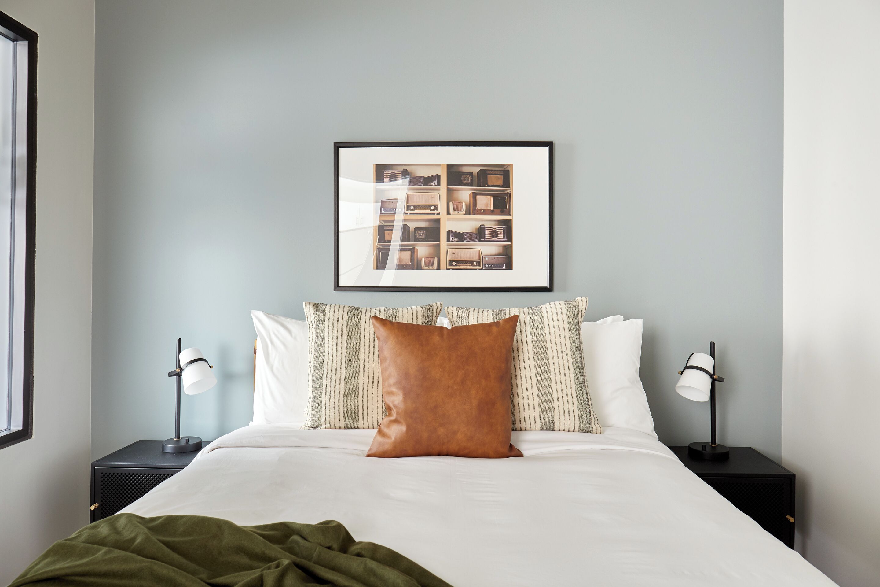 A neatly made bed with a brown pillow, two bedside lamps, and a framed picture above the bed.