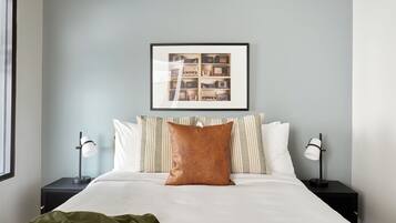 A neatly made bed with a brown pillow, two bedside lamps, and a framed picture above the bed.