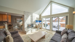 A spacious living area with a fireplace, large windows, and a view of a snowy deck. - Snake River 13 (Keystone)