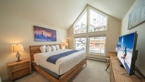 A bedroom with a large bed, a nightstand, a dresser, a TV, and a window with a view of buildings. - Snake River 13 (Keystone)