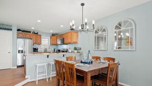 A modern kitchen with wooden cabinets, a central island, and a dining area with a wooden table and chairs. - Beach Paradise IX-Charming 4BR Townhouse•DOWNTOWN•Short walk to Beach&Boardwalk (Ocean City)