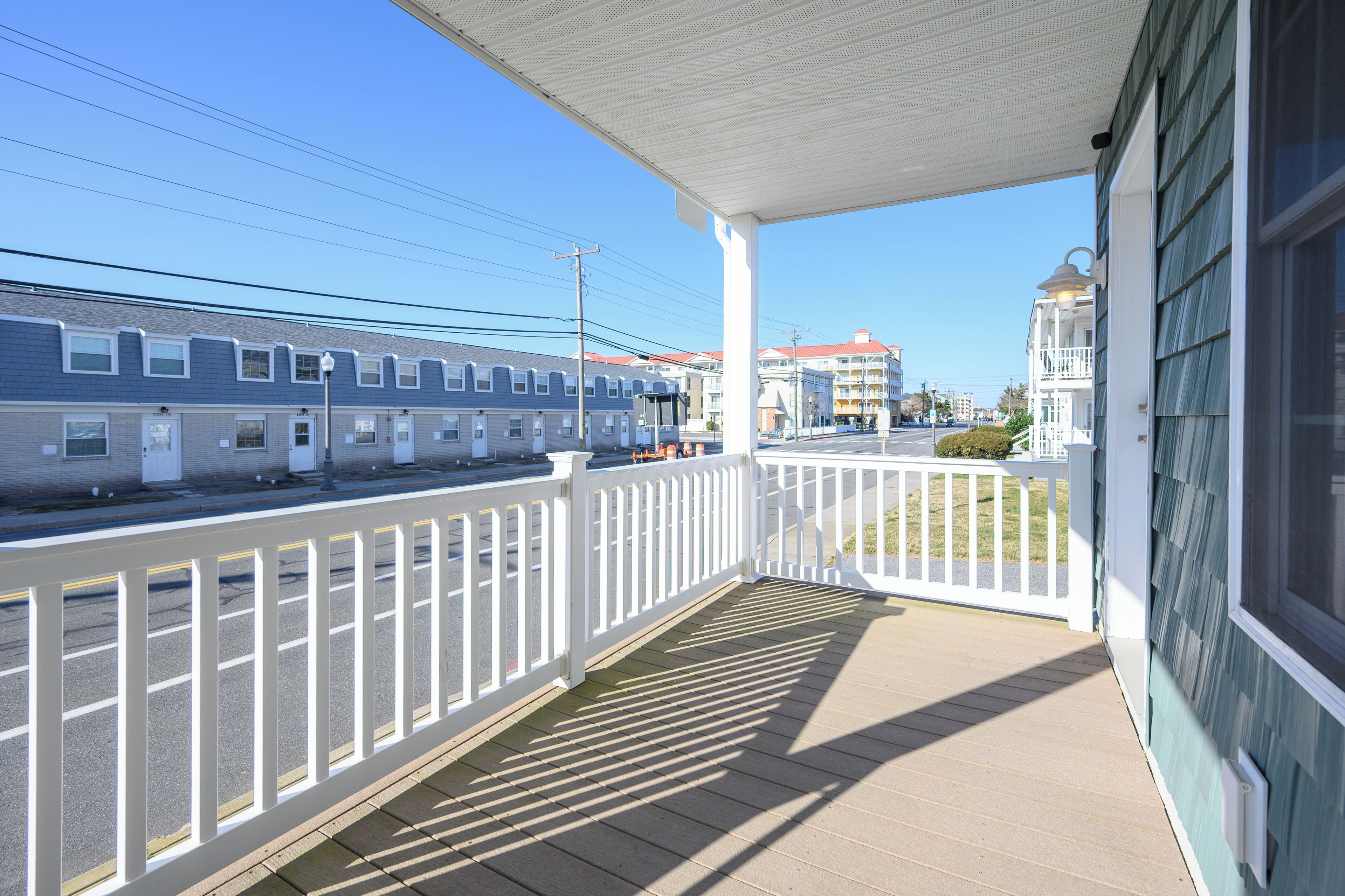 A covered porch with a white railing, overlooking a street with buildings and a train.