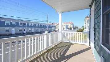 A covered porch with a white railing, overlooking a street with buildings and a train.