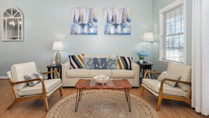 A living room with a beige sofa, two wooden chairs, a coffee table, and two paintings of sailboats. - Beach Paradise IX-Charming 4BR Townhouse•DOWNTOWN•Short walk to Beach&Boardwalk (Ocean City)