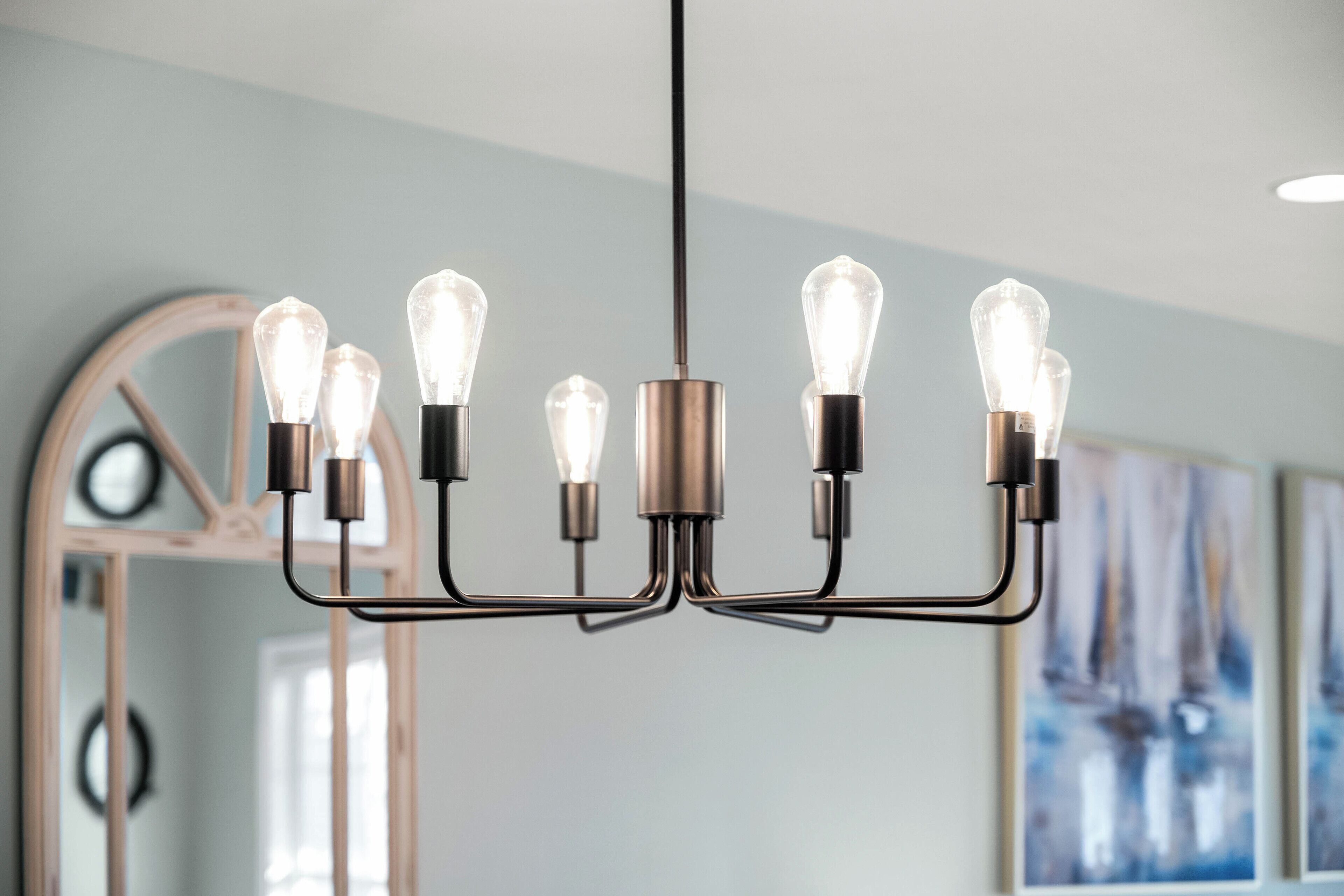 Een moderne kroonluchter met meerdere lampen in een kamer met een grote spiegel en abstracte kunst aan de muur.