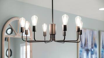 Een moderne kroonluchter met meerdere lampen in een kamer met een grote spiegel en abstracte kunst aan de muur.