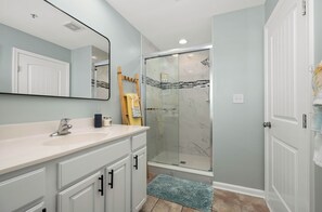 Un baño con tocador blanco, cabina de ducha de cristal y alfombra azul en el suelo.