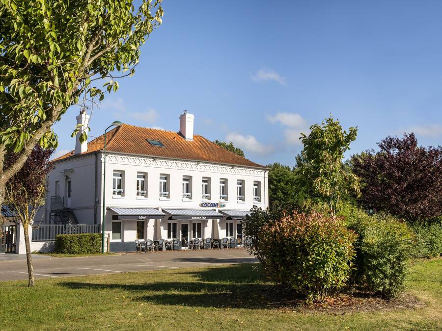 Un bâtiment blanc avec un toit rouge, de nombreuses fenêtres et une enseigne sur laquelle on peut lire « Hôtel Cococost ».