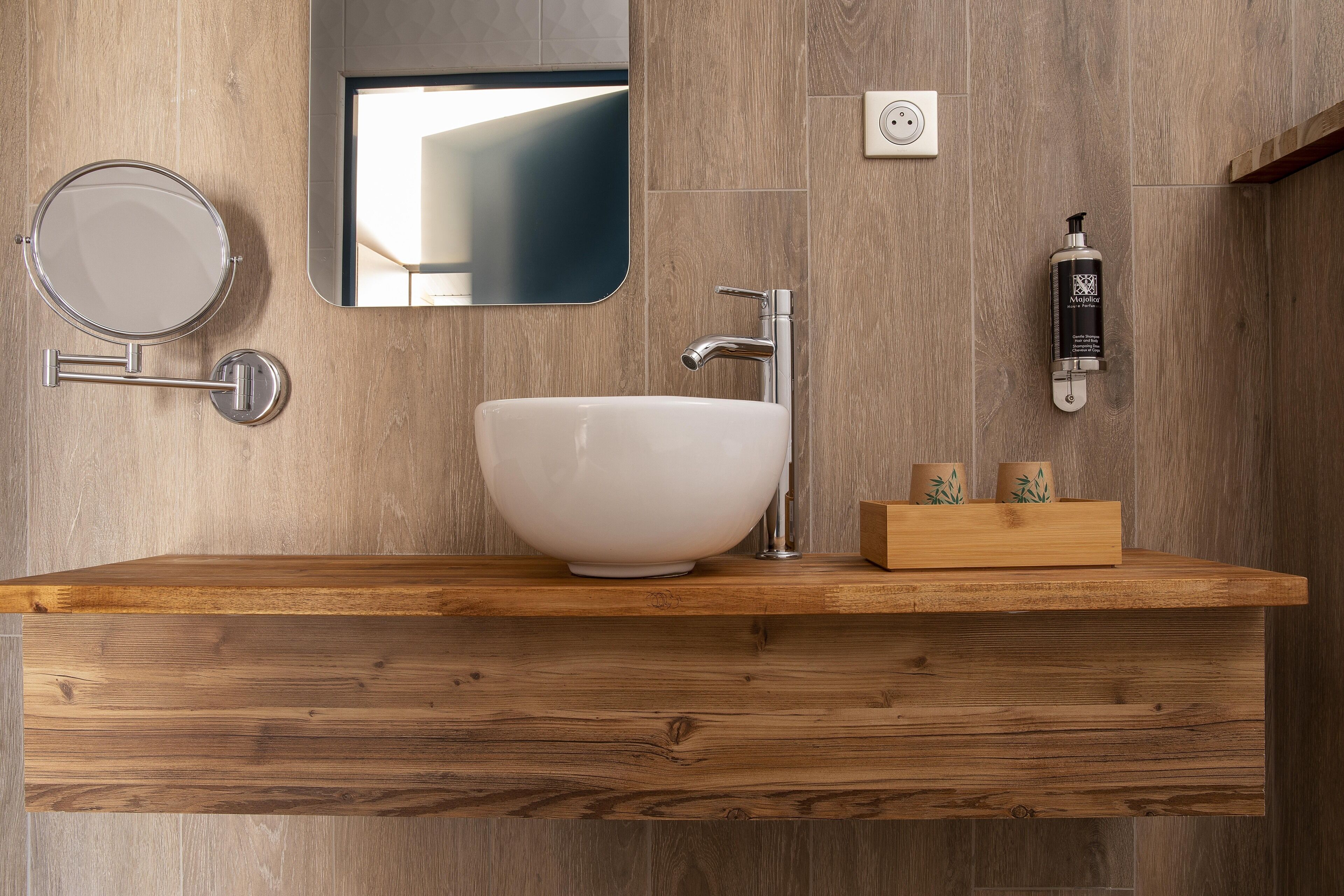 A modern bathroom with a wooden vanity, a round mirror, a white sink, a faucet, and a soap dispenser.