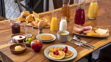 A breakfast table with pancakes, fruits, pastries, and beverages.