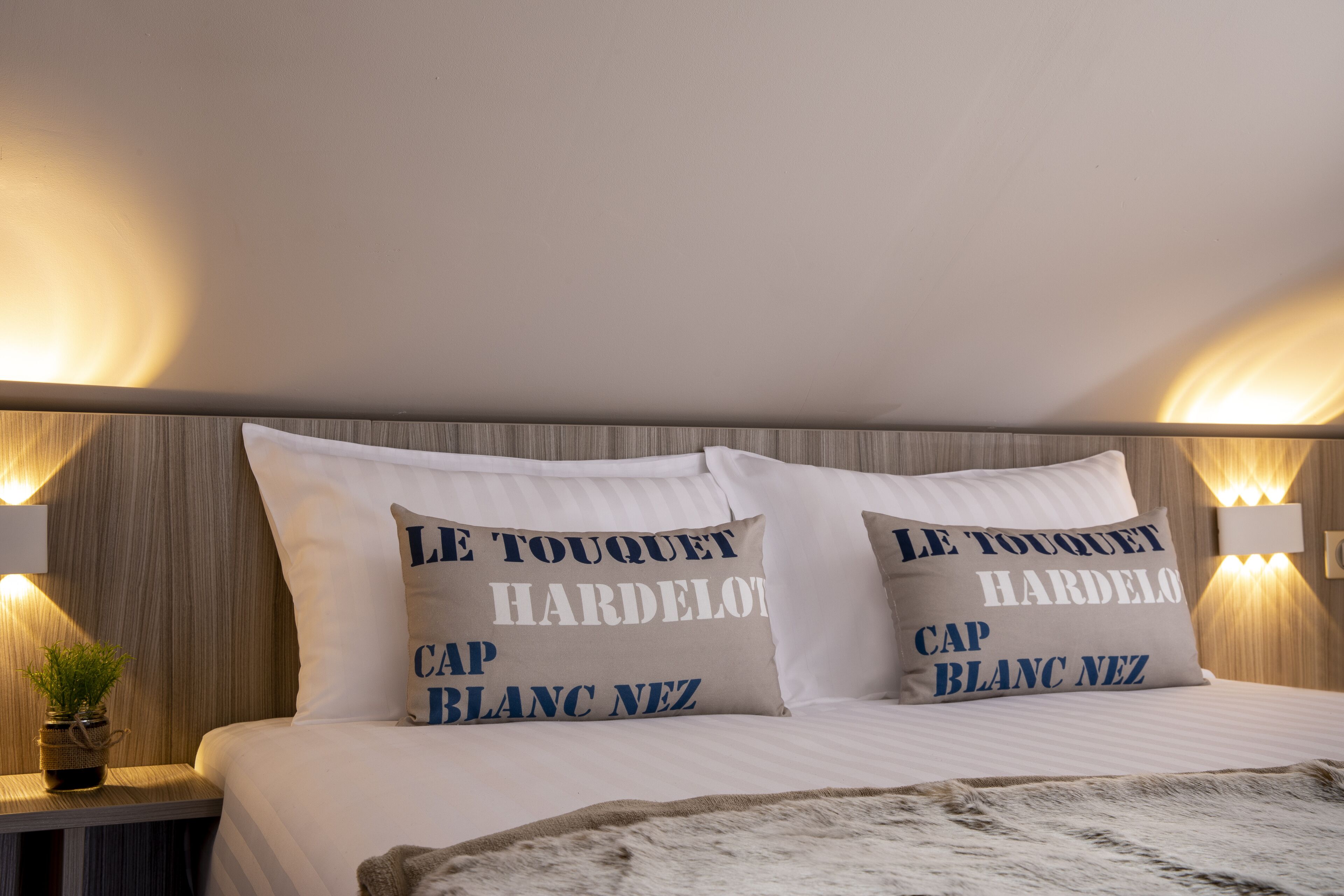 Una cama bien hecha con dos almohadas, cada una con texto en francés.