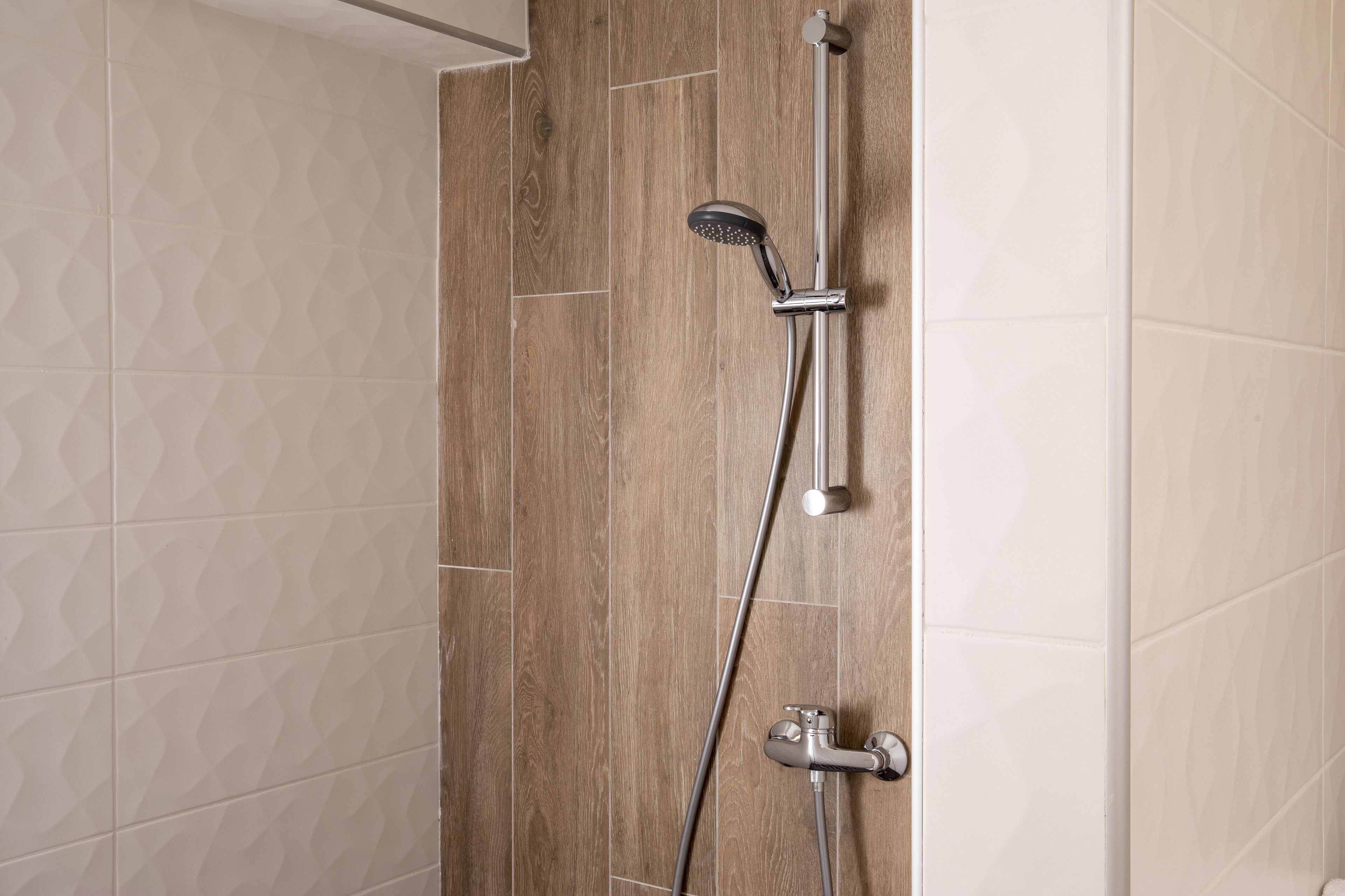 A shower with a handheld showerhead and a wall-mounted faucet.